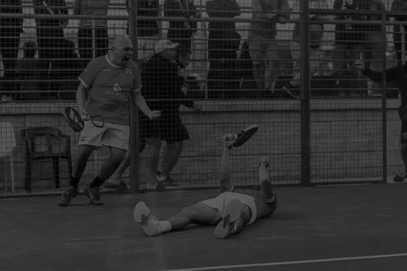 A padel player celebrates as his teammate lies on the court, capturing the emotional highs and intensity of the match.