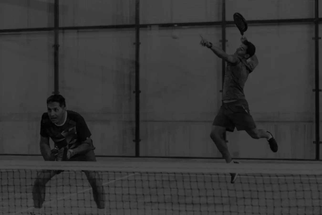 Two men playing padel, one jumping for an overhead smash while the other is positioned at the net, ready for the next move.