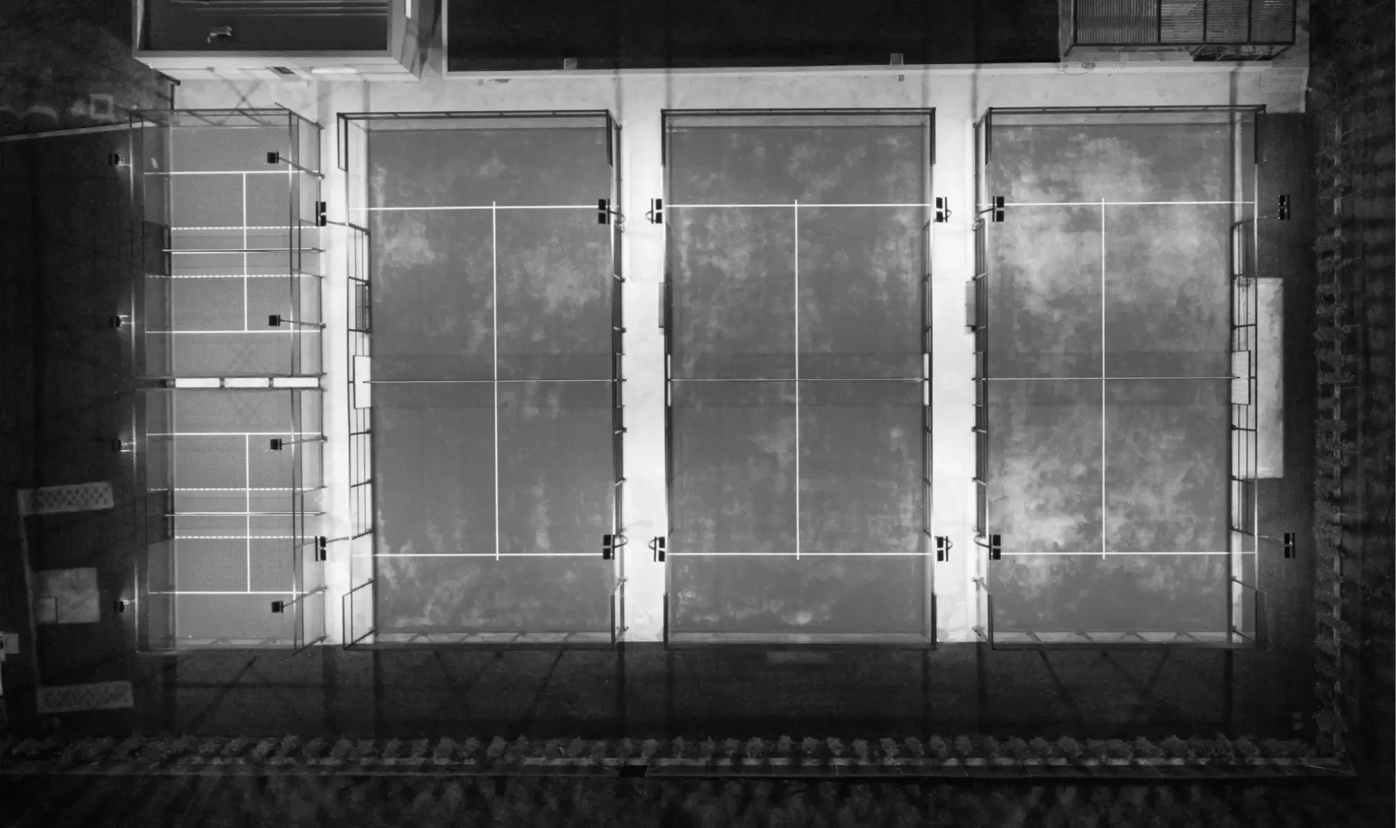 Top-down view of three illuminated padel courts at night, showcasing the distinct court lines and net structures.